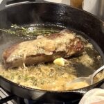steak cooked in a cast iron pan with roasted garlic and thyme sprigs